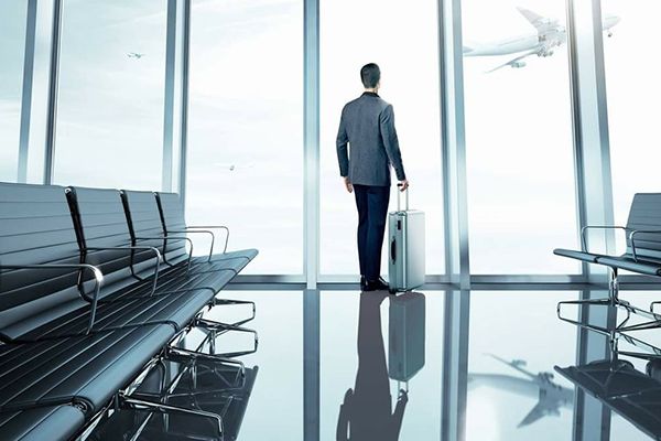 Man looking out an airport window holding a bag